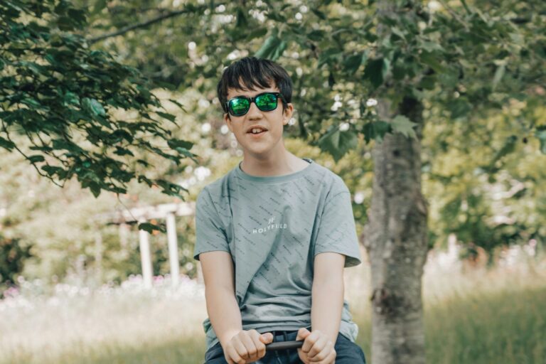 Teenage boy wearing sunglasses sitting outdoors in a garden, appearing calm and relaxed