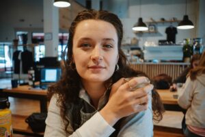 Young woman sitting in a café holding a drink, representing calm and emotional balance during homesickness with Neurofeedback