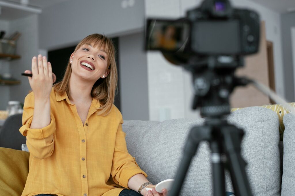 Woman recording content at home while smiling and speaking to a camera, appearing calm and engaged