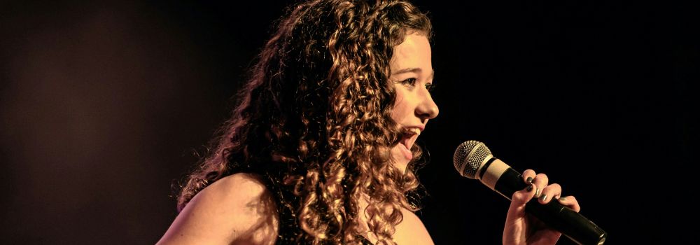 Woman performing on stage with a microphone, representing confidence and fewer performance nerves