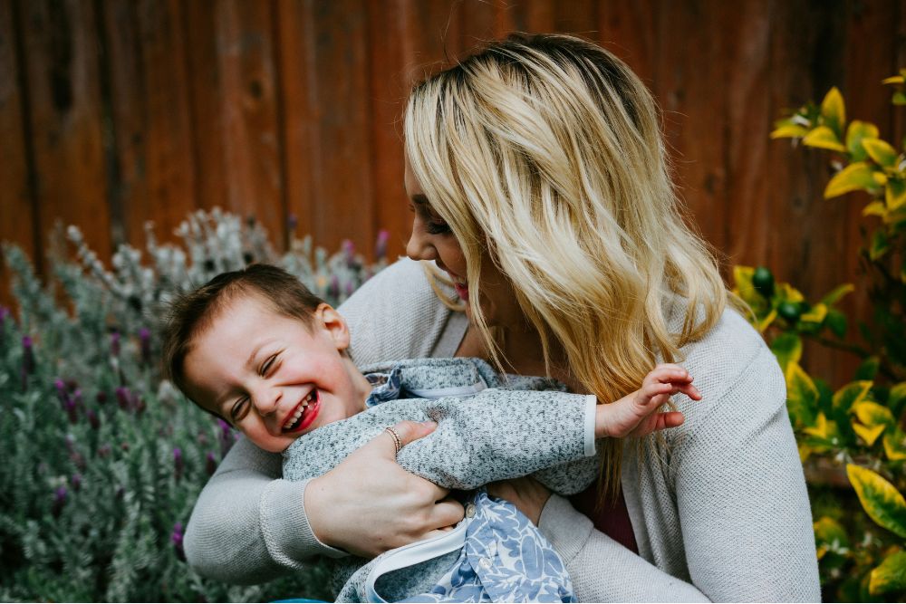 Mother holding her laughing child outdoors, representing connection, wellbeing and everyday life for NDIS participants