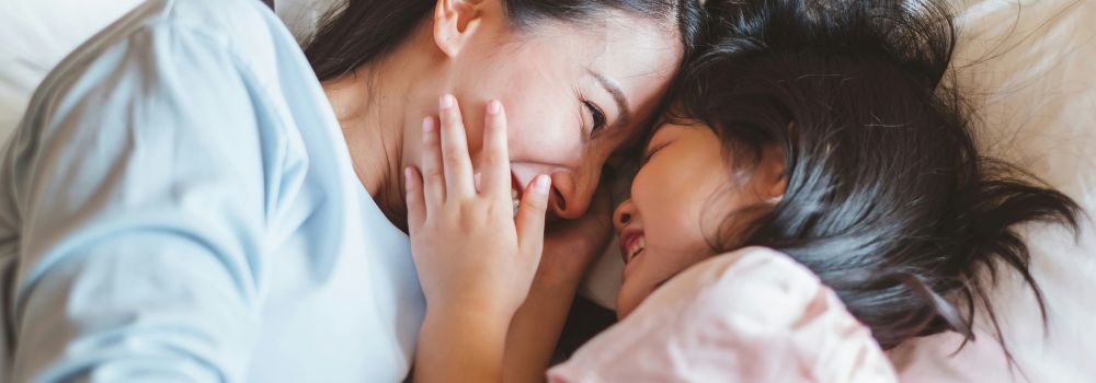 Mother and daughter laughing together in bed, representing a better mood after restful sleep