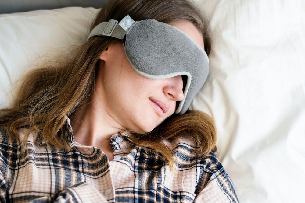Woman resting in bed with a sleep mask, representing sleep and fatigue