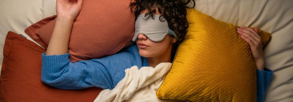 Woman resting in bed with a sleep mask, representing less overthinking at night