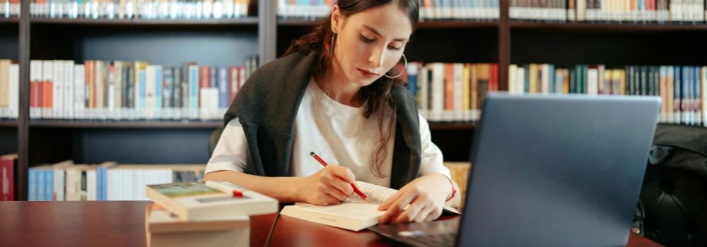 Student studying with books and a laptop in a library
