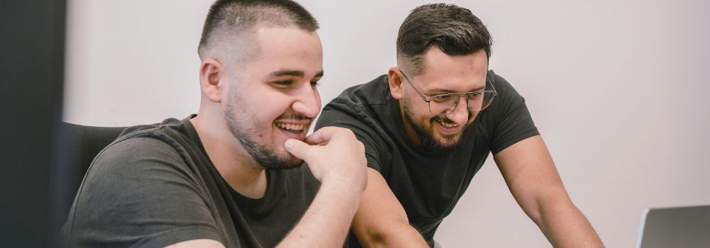 Two male colleagues smiling while working together, representing calm leadership, positive communication and workplace relationships