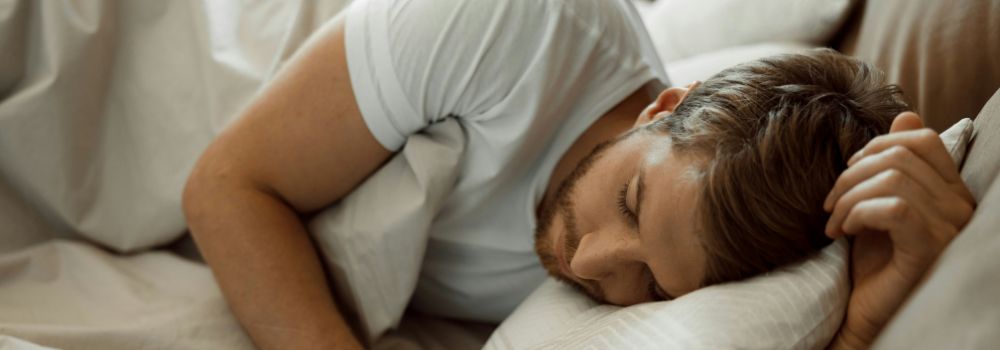 Man sleeping peacefully in bed, representing better sleep quality, recovery and improved wellbeing